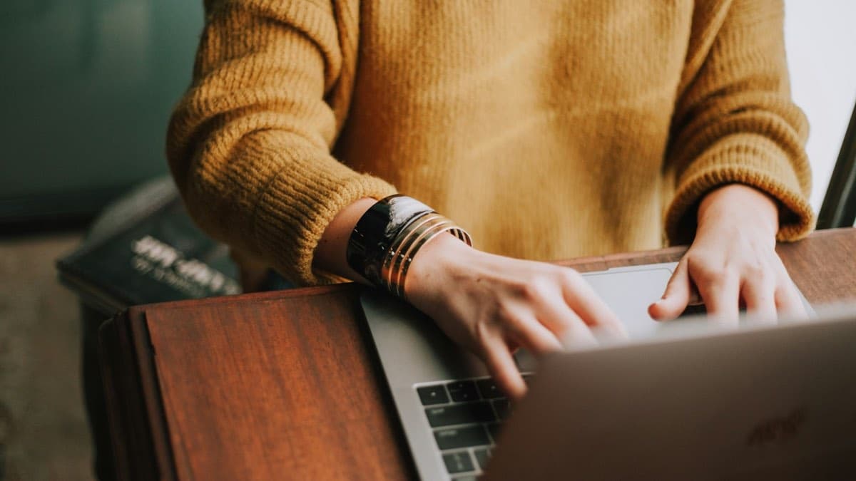 Practice owner typing on a laptop at a wooden desk, the ongoing work of keeping a therapy website and Google profile visible to new clients